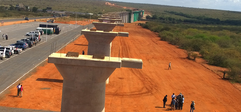 A photo showing the pillars of the 2 km Tsavo River Super Bridge for new Standard Gauge Railway situated within the Tsavo National Park. The bridge has 60 spans with 32m long for each span. The tarmac road on the extreme left is the Nairobi-Mombasa highway separating Tsavo West and East National Parks to the left and to the right respectively. This section of the road should be raised to the height of the Tsavo River Super Bridge to allow for undisturbed movement of wildlife and minimise wildlife road kills